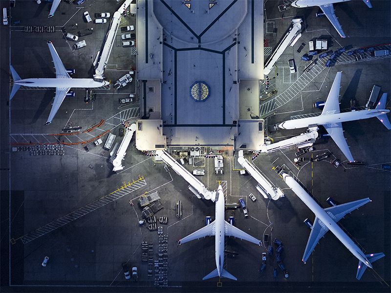 Aerial view of airliners, staff, vehicles, ramps, gates and the Control Tower at LAX airport lit up at night.